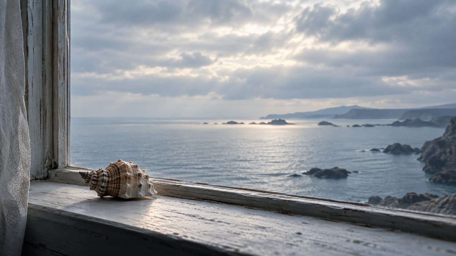Una concha marina pequeña sobre el alféizar de una ventana con vista al mar en calma, con luz difusa de tarde nublada.